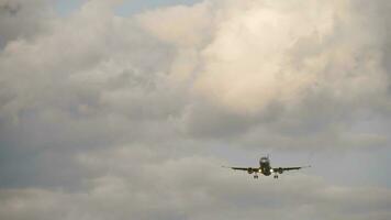 Airplane approaching landing. Commercial airliner flies in the gray cloudy sky, front view, long shot. Air travel and tourism concept video