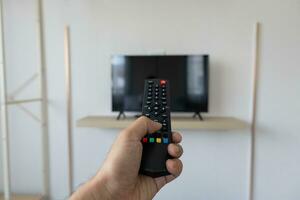 Close up Television remote control in hand man pointing to tv set and turning it on or off. select channel watching tv at home in the living room relax. photo