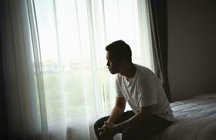 Silhouette depressed man sadly sitting on the bed in the bedroom. Sad asian men suffering depression insomnia awake and sit alone on the bed in bedroom. Depression health people concept. photo