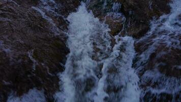 A close-up aerial view of a mountain river with white splashes of water cascading down a rocky shore. A mountain river with fast-flowing water video