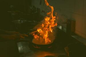 Chef cooking and doing flambe on food in restaurant kitchen photo