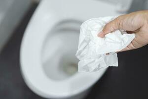 close up hand holding a tissue to be thrown into the toilet bowl. Can not drain water of toilet paper in the toilet bowl cause the stool to clog up. photo