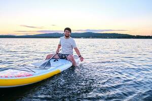 A man sits on a paddle board at sunset. photo