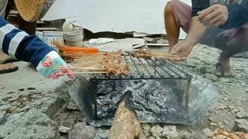 Villagers are grilling goat meat satay that has been smeared with spices using a simple grill and wood charcoal in the morning. video