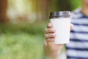 mano sosteniendo una taza de papel para llevar bebiendo café a la luz del sol natural de la mañana. lugar de espacio para su logotipo. dejar espacio para escribir texto. foto