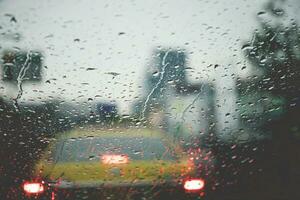 Drops Of Rain Drizzle on the glass windshield in the evening. street in the heavy rain. Bokeh Tail light and Traffic lights in city. Please drive  car carefully, slippery road. soft focus. photo