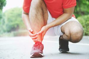 lesión desde rutina de ejercicio concepto el asiático hombre utilizar manos sostener en su rodilla mientras corriendo en la carretera en el parque. Disparo en Mañana tiempo, luz de sol y calentar efecto con Copiar espacio para texto o diseño foto