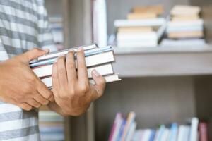close up student young man hand holding books are placed front bookshelf in a library University. love to read education concept. with filter Tones retro vintage warm effect. photo