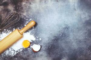 dough preparation recipe bread. Baking ingredients bakery cooking. egg yolk,Egg whisk,rolling pin and flour on black board. flat lay on table dark background. Top view, copy space. photo