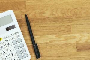 top view of black pen with calculator on vivid office desk table wooden background table for business with blank copy space, math, cost, tax or investment calculation. photo