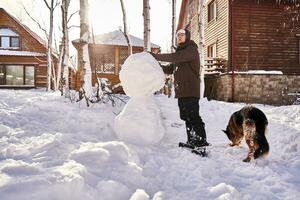 un familia construye un monigote de nieve fuera de blanco nieve en el yarda en invierno. foto