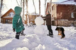 A family builds a snowman out of white snow in the yard in winter. photo