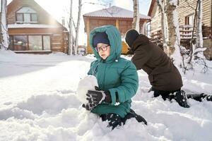 un familia construye un monigote de nieve fuera de nieve en el yarda en invierno. foto