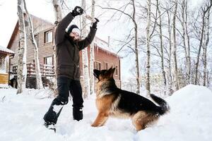 A man plays fetch with a dog in the snowy yard of a house. photo