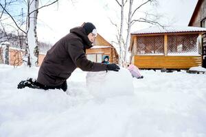 A family builds a snowman out of white snow in the yard in winter. photo