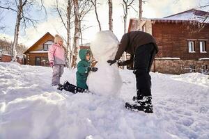 A family builds a snowman out of white snow in the yard in winter. photo