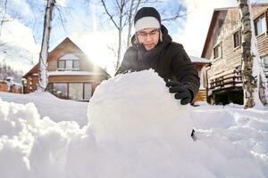 un familia construye un monigote de nieve fuera de nieve en el yarda en invierno. foto