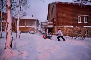 un joven hombre borra nieve con un nieve soplador en su patio trasero. foto