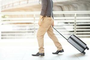 businessman walking outside public transport building with luggage in rush hour. Business traveler pulling suitcase in modern airport terminal. baggage business Trip. photo