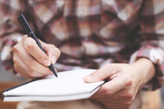 close up hand young man are sitting using pen writing Record Lecture note pad into the book on the table wood. photo