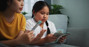 retrato de joven mujer y adolescente niña contando efectivo dinero en sofá en el vivo habitación a en casa, feliz contando dolares billete foto