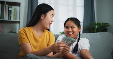 retrato de joven mujer y adolescente niña contando efectivo dinero en sofá en el vivo habitación a en casa, feliz contando dolares billete foto