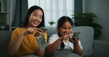 Portrait of a young woman and teenage girl enjoying scattering cash bills on a sofa in the living room at home. photo