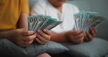 retrato cerca arriba de joven mujer y adolescente niña contando efectivo dinero en sofá en el vivo habitación a en casa, feliz contando dolares billete foto