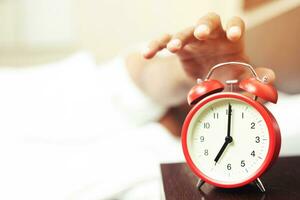 Close up of man lying in bed turning off hand reaching out for alarm clock color black Wake up late at morning at 7.20 am. photo