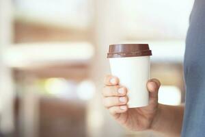 mano sosteniendo una taza de papel para llevar bebiendo café a la luz del sol natural de la mañana. lugar de espacio para su logotipo. dejar espacio para escribir texto. foto