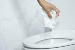 close up hand holding a tissue to be thrown into the toilet bowl. Can not drain water of toilet paper in the toilet bowl cause the stool to clog up. photo