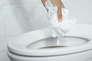 close up hand holding a tissue to be thrown into the toilet bowl. Can not drain water of toilet paper in the toilet bowl cause the stool to clog up. photo