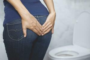 portrait of a woman suffers from diarrhea his stomach painful. ache and problem. hand hold tissue paper roll in front of toilet bowl. constipation in bathroom. Hygiene, health care concept. photo