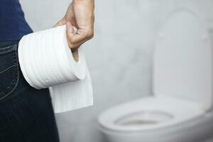 portrait of a woman suffers from diarrhea his stomach painful. ache and problem. hand hold tissue paper roll in front of toilet bowl. constipation in bathroom. Hygiene, health care concept. photo