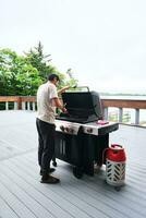 un hombre cocineros en un parrilla en el veranda. foto