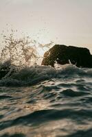 olas estrellarse en el rocas a puesta de sol foto