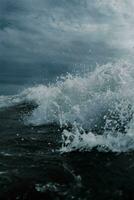 a wave crashing on the ocean with a cloudy sky photo