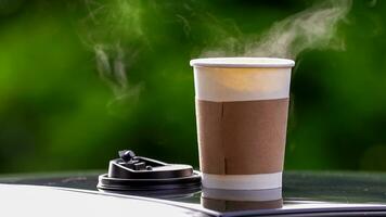 café para llevar en un papel taza en parte superior de el coche techo verde árbol antecedentes a amanecer en el mañana, selectivo enfocar, suave enfocar. foto