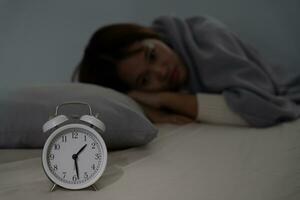 asiático mujer en cama tarde molesto a dormir sufrimiento insomnio, insomne o asustado en un pesadilla, mirando triste preocupado y estresado. cansado y dolor de cabeza o migraña despertar arriba en el medio de el noche. foto