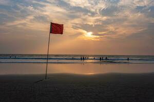 red flag on beach on sea or ocean at sunset as symbol of danger. The sea state is considered dangerous and swimming is prohibited. photo