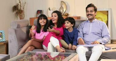 Indian family watching football match on TV together at home  sitting on sofa in living room video