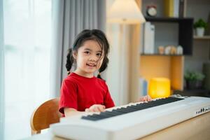 contento pequeño asiático linda bebé niña sonrisa jugando aprendizaje en línea piano música en vivo habitación a hogar. el idea de ocupaciones para niño a hogar durante cuarentena. música aprendizaje estudiar. foto