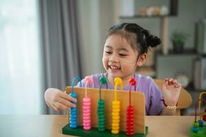 Young cute Asian baby girl is learning the abacus with colored beads to learn how to count on the table in the living room at home. Child baby girl development studying concept. photo