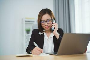 Freelance business woman calling on mobile smartphone while working with laptop, businesswoman mobile phone to calling with customers or shopping online. Smart phone conversation conferrence. photo