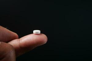 closeup of a medical tablet on a finger on black background photo