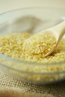 raw bulgur with wooden spoon in a bowl on table photo