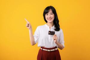 retrato hermosa joven asiático mujer emprendedor contento sonrisa vistiendo blanco camisa y rojo plantas señalando dedo gesto a gratis Copiar espacio y participación crédito tarjeta aislamiento en amarillo antecedentes. foto