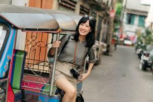 Young Asian woman backpack traveler standing a side of Tuk Tuk taxi on summer vacations at Bangkok, Thailand. photo
