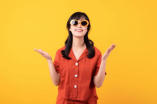 Portrait young beautiful asian woman happy smile dressed in orange clothes showing hand gesture, arm compare two variants demonstrate empty space isolated on yellow studio background. photo