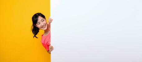 young asian sports fitness woman happy smile wearing pink sportswear standing behind the white blank banner or empty space advertisement board against yellow background. wellbeing lifestyle concept. photo